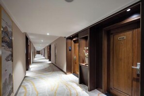 Un couloir d’hôtel avec des portes en bois, un sol en marbre et un panneau fixé au mur.