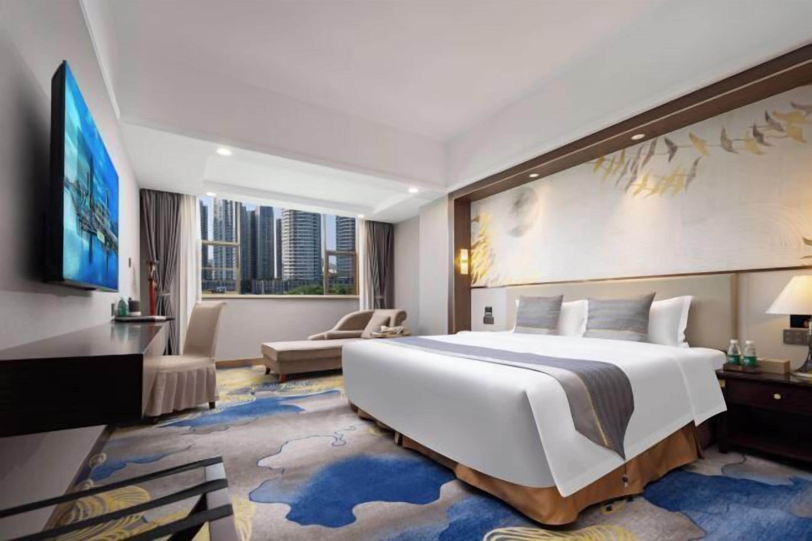 Une chambre d’hôtel avec un grand lit, un bureau, une chaise et une vue sur le panorama urbain.