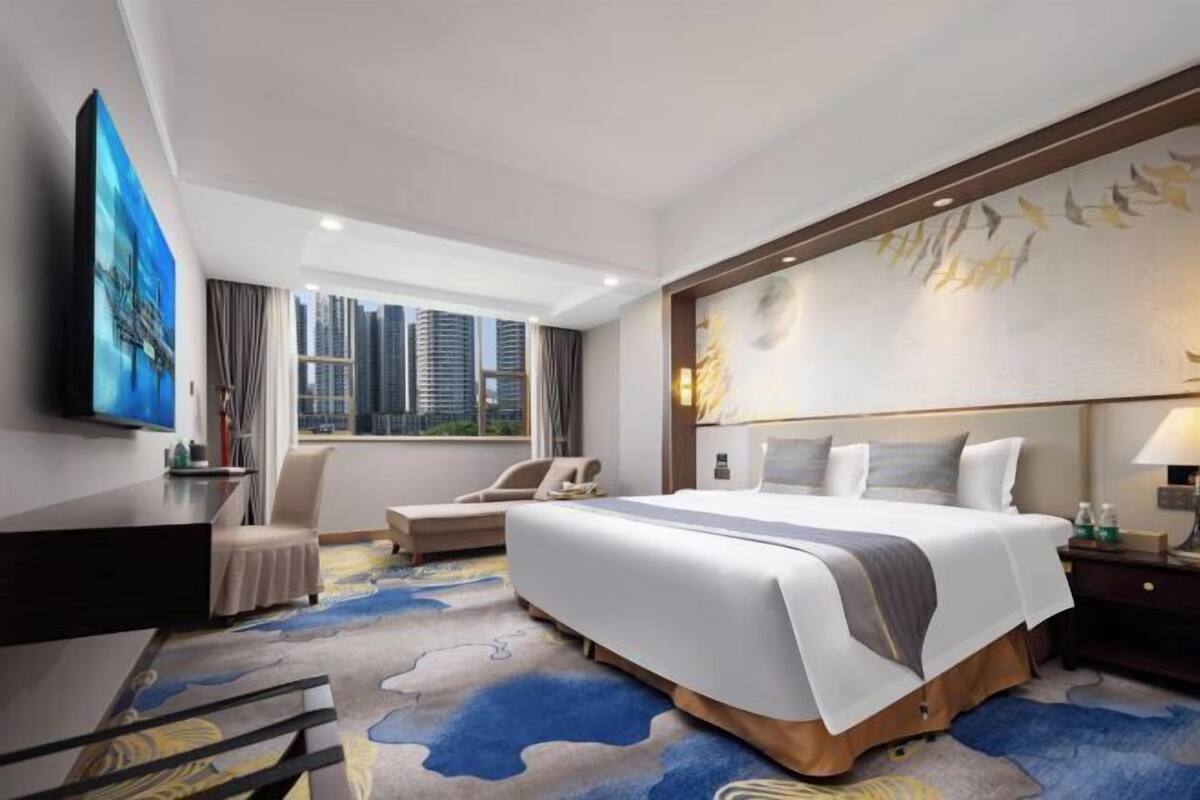 A hotel room with a large bed, a desk, a chair, and a view of the city skyline.