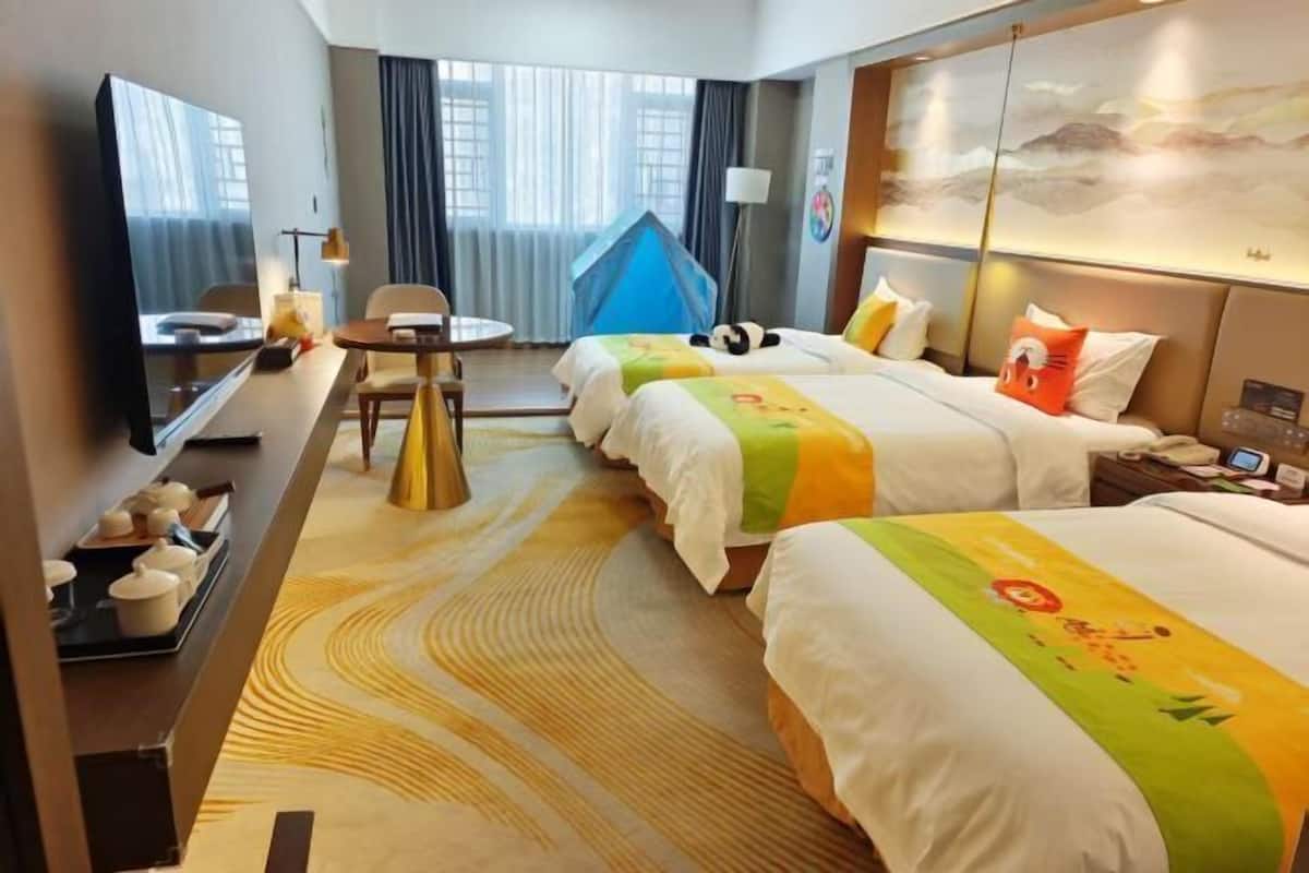 A hotel room with two beds, a desk, a chair, a TV, and a large window with curtains.