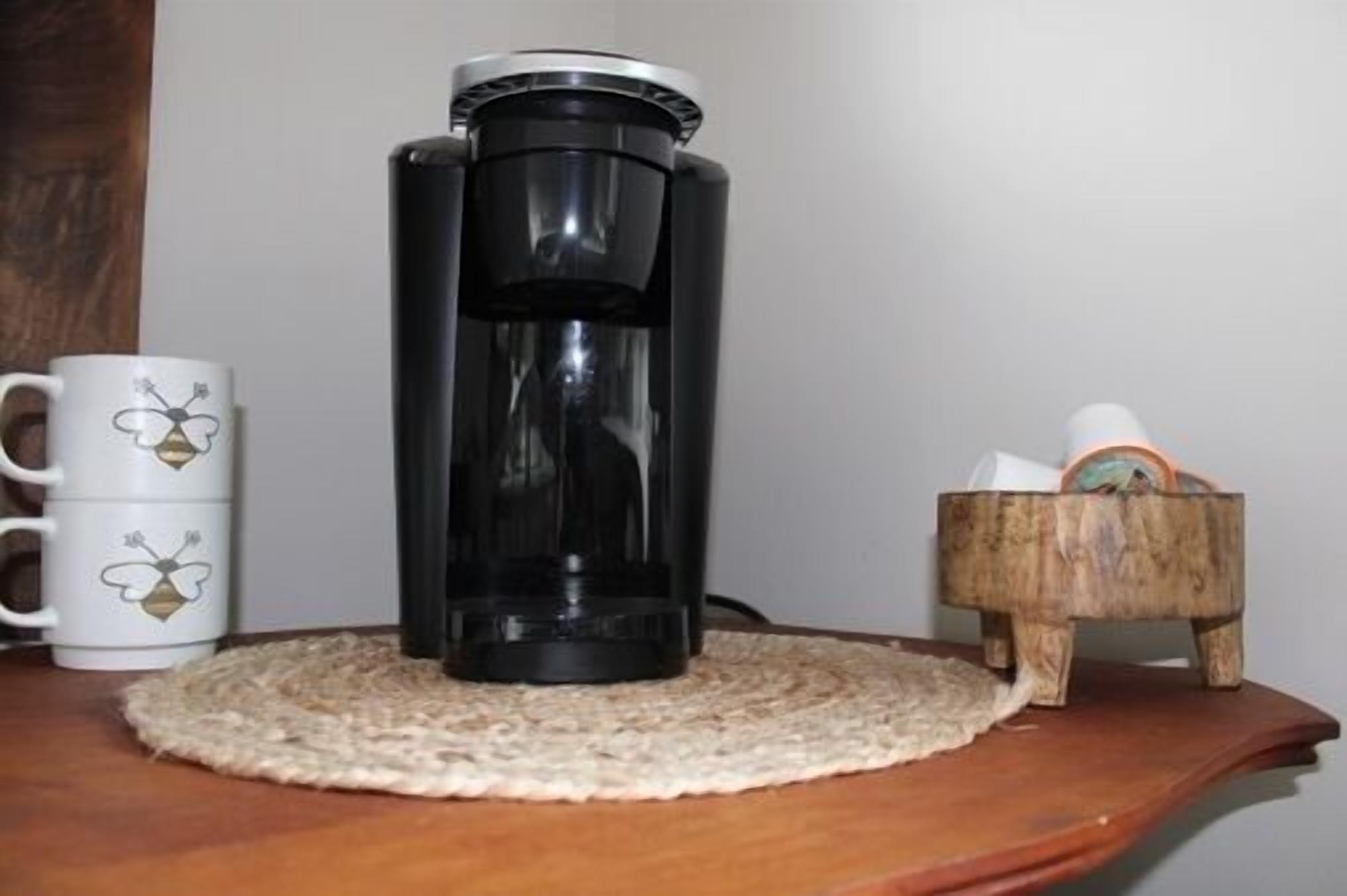 A coffee maker on a wooden table with a woven placemat.