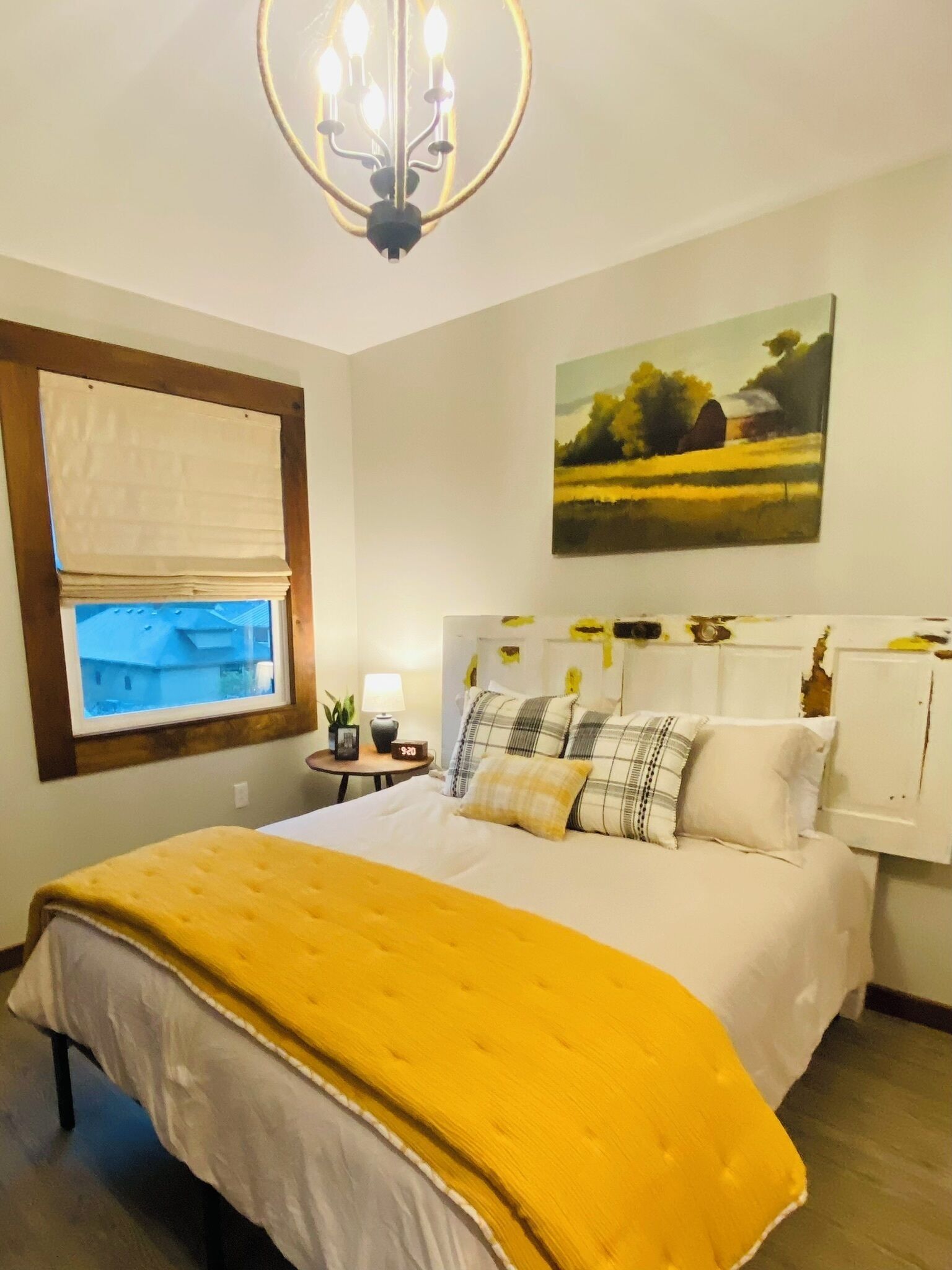 Un dormitorio con cama, ventana con vistas, un cuadro y una araña.