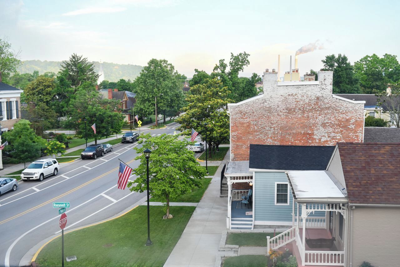 A street view with a brick building, a small porch, and a flag on the sidewalk.