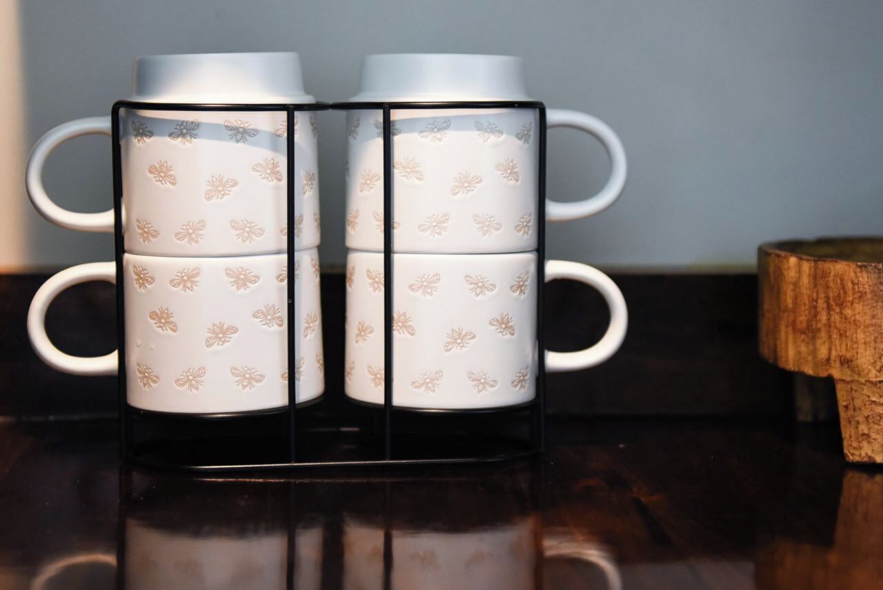 A set of four white ceramic mugs with floral patterns, arranged in a black holder on a reflective surface.