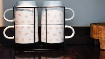 A set of four white ceramic mugs with floral patterns, arranged in a black holder on a reflective surface.