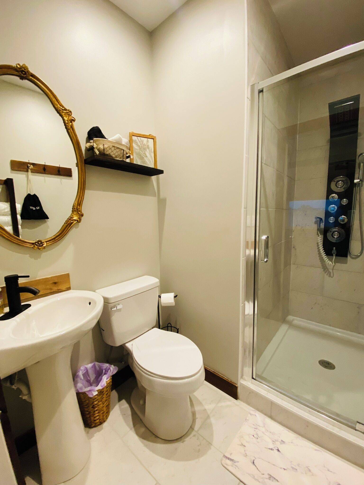 A bathroom with a white toilet, a sink, a mirror, a shower, and a small shelf with toiletries.