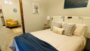 A bedroom with a bed, a nightstand, a lamp, a chair, and a painting on the wall. - The Madison Inn, Historic woodside view suite 205, Historic woodside view suite 205 (Madison)