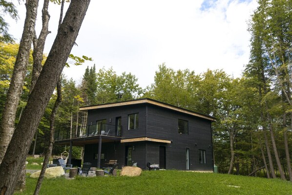 Une maison moderne à deux étages, dotée d’un balcon et entourée d’arbres.