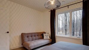 Et soveværelse med seng, sofa, vindue med udsigt til træer og en hængende lampe.