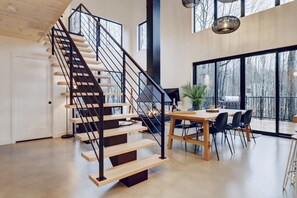 A modern interior with a wooden staircase, a dining area, and large windows. - Pur Nature Eastman et Spa (Eastman)