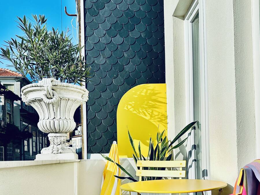 A balcony with a yellow chair, a small table, and a potted plant.