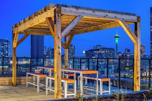A wooden pergola structure with benches on a rooftop terrace overlooking a cityscape at dusk. - Downtown Calgary Oasis (Calgary)