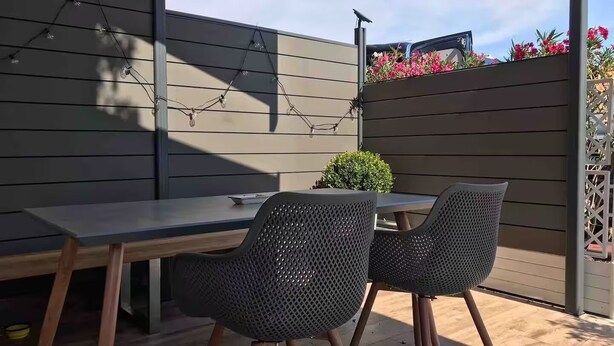 Eine Terrasse im Freien mit Tisch, zwei Stühlen, einem kleinen Topfpflanzen und einer Lichterkette.