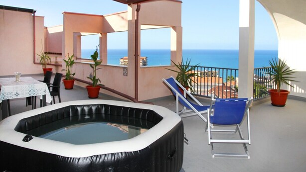 A rooftop terrace with a hot tub, lounge chairs, and potted plants.
