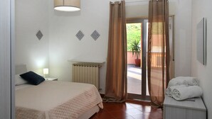 A bedroom with a bed, a radiator, a window with curtains, and a small table with towels.
