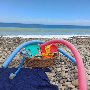 A beach scene with a wicker basket containing beach toys and a blue towel on the pebbled shore. - Tenuta Piana 1: Direct Access to the sea (Caronia)