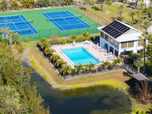 Vista aérea de un complejo turístico con dos canchas de tenis, una piscina y un edificio con paneles solares.