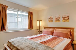Un lit bien fait, recouvert d’une couvre-lit à motifs, une table de chevet, une lampe sur pied et une fenêtre avec des rideaux.