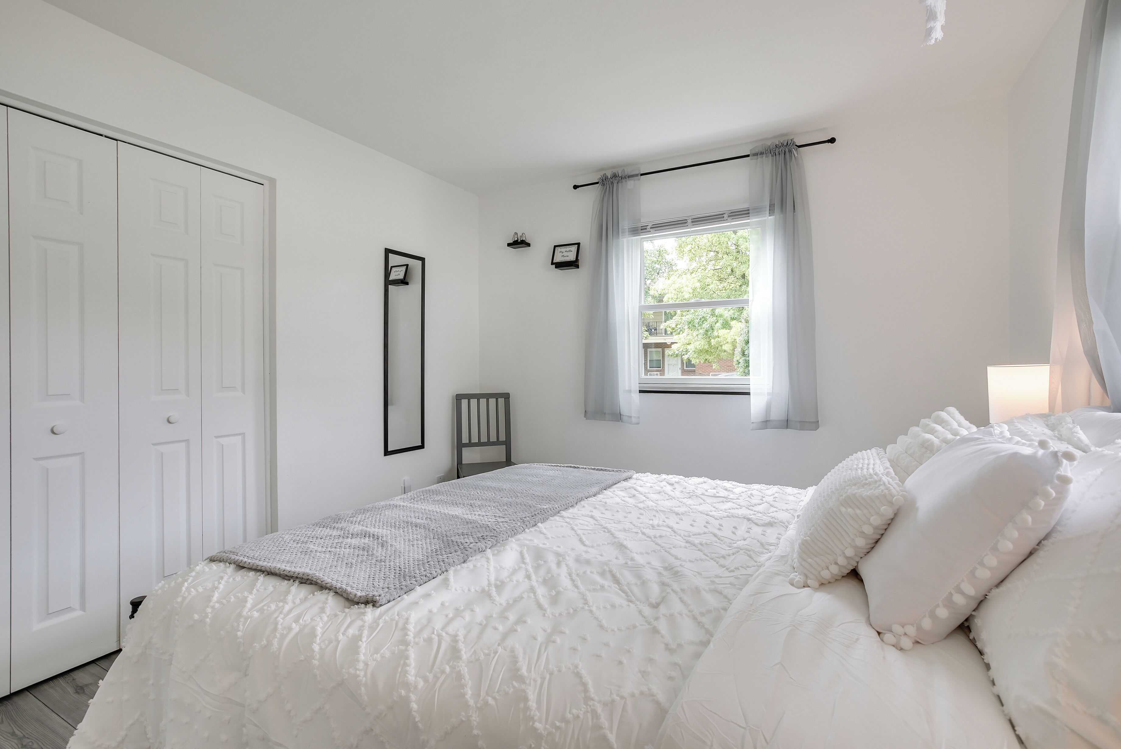 A bedroom with a large bed, a window with curtains, a wardrobe, and a framed picture on the wall.