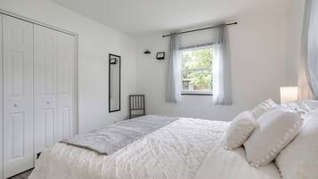 A bedroom with a large bed, a window with curtains, a wardrobe, and a framed picture on the wall.