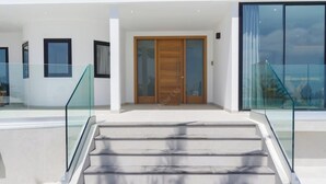 Une entrée moderne, avec un escalier en verre, une porte en bois et une rambarde en verre.