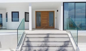 A modern building entrance with a glass staircase, a wooden door, and a glass railing.