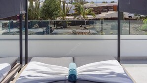 Un balcon avec une balustrade en verre, un lit avec du linge de lit blanc et une serviette bleue.