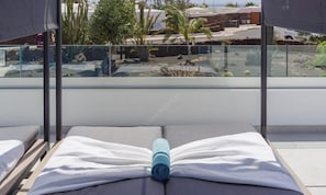 A balcony with a glass railing, a bed with white bedding, and a blue towel.