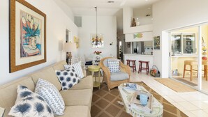 A living room with a sofa, armchairs, a dining table, and a kitchen area visible through an open door.