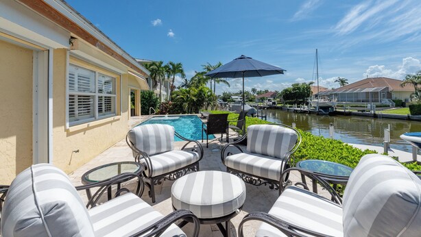 A poolside area with outdoor furniture, a view of a canal, and a building with a beige facade.