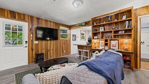 A cozy living room with a TV, wooden shelves, a dining table, and a couch. - Charming Serene Cabin in Nantahala Gorge near Bryson City (Bryson City)