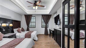 Camera d'albergo con due letti, una scrivania, una ventola a soffitto e un'ampia finestra.