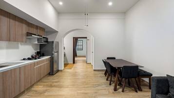 Una cocina moderna con armarios de madera, un refrigerador de acero inoxidable y un microondas. Hay un comedor con una mesa y sillas, y un sofá.