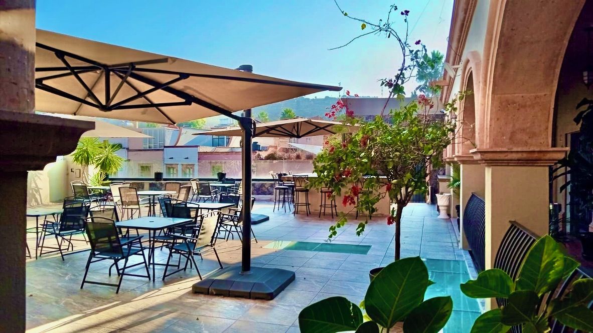 Un espacio de patio al aire libre con mesas y sillas, una zona de estar cubierta y plantas en macetas.