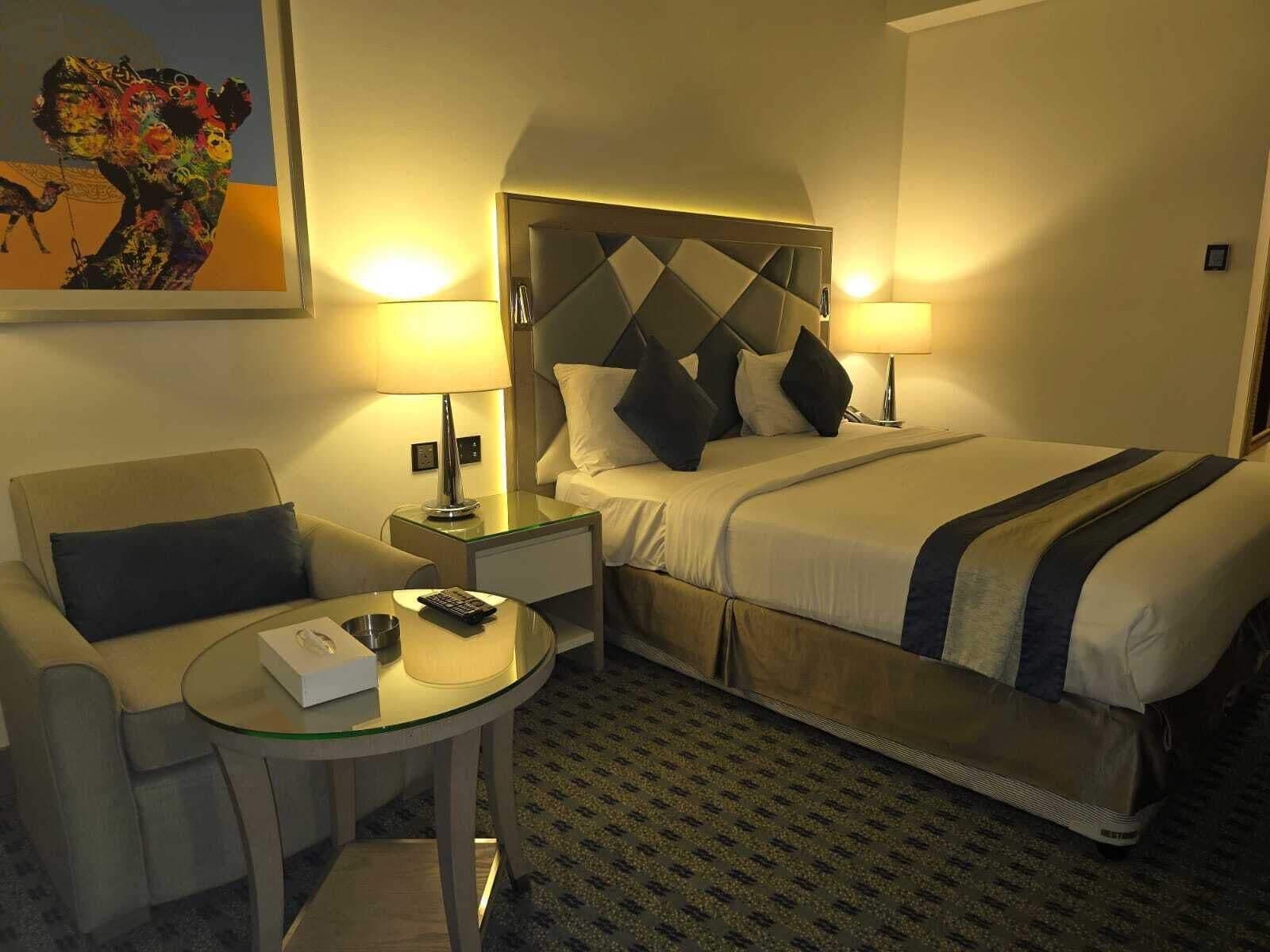 A hotel room with a bed, a sofa, a small table, and a painting on the wall.
