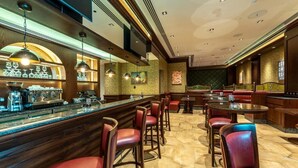 Una zona de bar con una barra larga, varios taburetes y un área de estar con mesas y sillas.