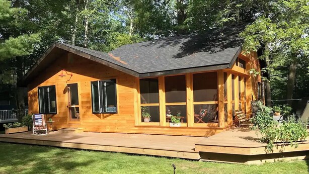 A wooden cabin with a porch, large windows, and a small deck area.
