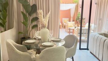A dining area with a glass table, four chairs, and a vase with white flowers.