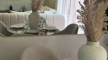 A dining area with a modern table set for two, a vase with dried plants, and a large mirror reflecting the room.