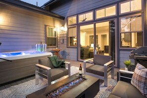 A modern outdoor living area with a hot tub, seating, and a fire feature.