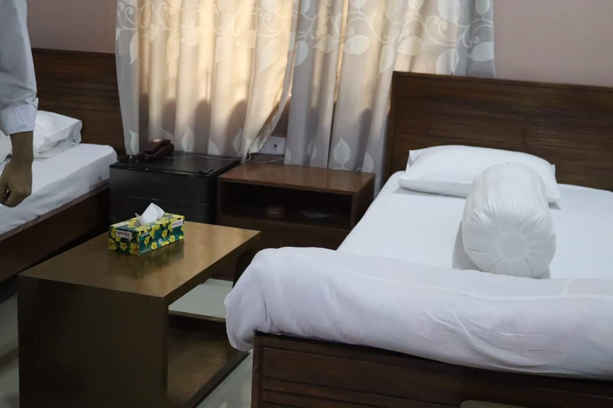 Habitación de hotel con dos camas, una mesita de noche con caja de pañuelos y otra con un teléfono, y un cabecero de madera.