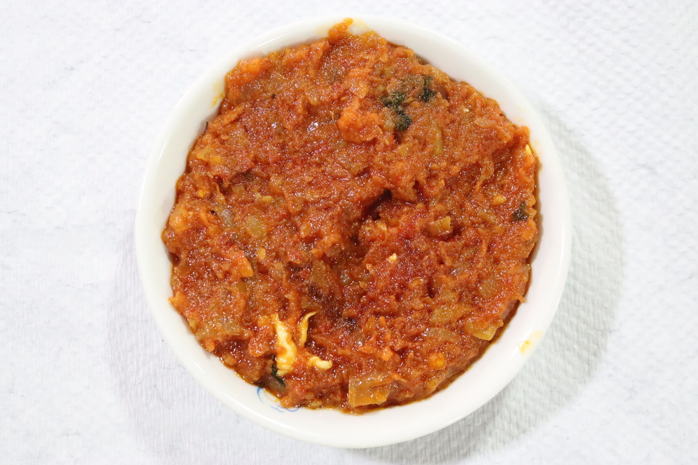 Een kom rode saus met zichtbare kruiden en stukjes, mogelijk een soort chutney of relish.