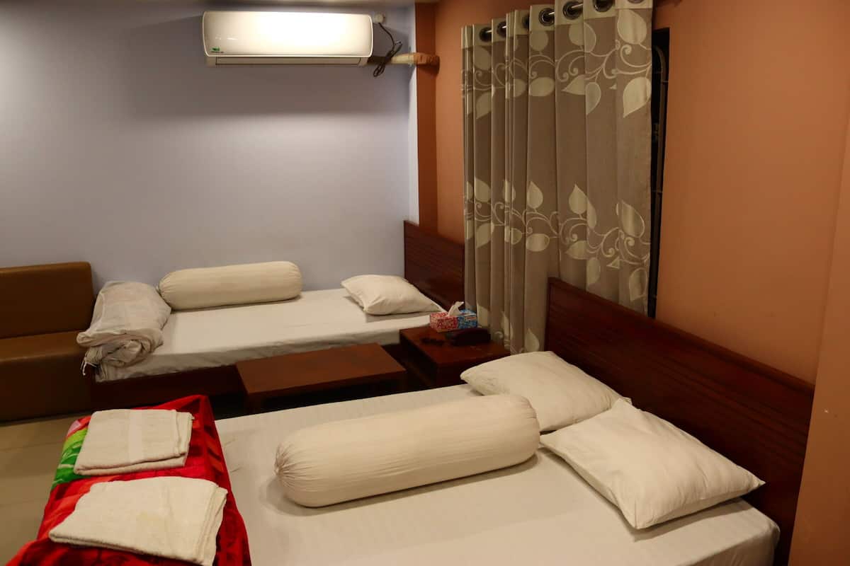 Habitación de hotel con dos camas, un sofá, cabecera de madera, toalla roja y aire acondicionado de pared.