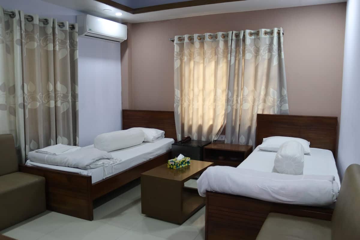 Habitación de hotel con dos camas, cabecera de madera, una mesita y una mesita de noche.