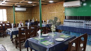 Een restaurant met tafels met blauwe tafelkleden, houten stoelen en een ventilator.