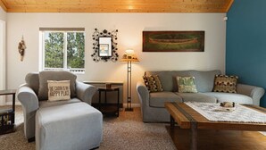 A cozy living room with a sofa, a chair, a coffee table, a lamp, and a painting on the wall. - Blissful Bay Cabin + Block from Boulder Bay (Big Bear Lake)