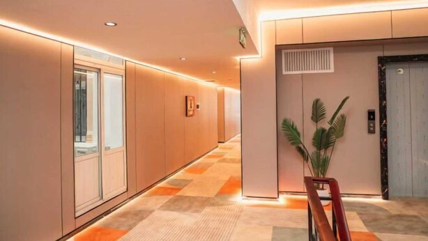 Un couloir d’hôtel moderne avec un sol à carreaux, une plante en pot et un ascenseur.
