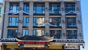 Un immeuble à plusieurs étages présentant des éléments d’architecture chinoise traditionnelle, notamment des colonnes richement décorées et une façade recouverte de carreaux.