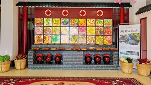 L’intérieur d’un restaurant présente un décor de style chinois traditionnel, avec un mur orné de photos colorées de plats, une sélection de bouteilles de vin rouge et des éléments décoratifs tels que des lanternes et des fleurs.