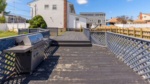 Une terrasse en bois avec un barbecue et une vue sur des immeubles d’habitation.